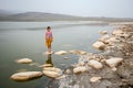 A child girl in a striped T-shirt and a yellow skirt is standing on a stone in the water in the lake. Royalty Free Stock Photo