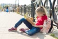 Child girl student wearing glasses with backpack is reading book. Urban background, river, sky. Royalty Free Stock Photo