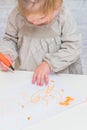 Child, a girl at the table writes, draws on a piece of paper, against a white brick wall Royalty Free Stock Photo