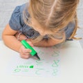 Child, a girl at the table writes, draws on a piece of paper, against a white brick wall Royalty Free Stock Photo