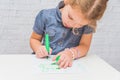 Child, a girl at the table writes, draws on a piece of paper, against a white brick wall Royalty Free Stock Photo