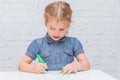 Child, a girl at the table writes, draws on a piece of paper, against a white brick wall Royalty Free Stock Photo