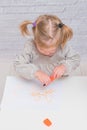 Child, a girl at the table writes, draws on a piece of paper, against a white brick wall Royalty Free Stock Photo