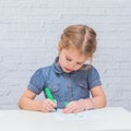 Child, a girl at the table writes, draws on a piece of paper, against a white brick wall Royalty Free Stock Photo