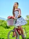 Child girl wearing white polka dots dress rides bicycle .