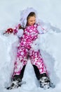 Child girl wearing winter clothes lying in snow .