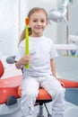 Child girl in white clothes at reception at a pediatric dentist smiles and laughs. little girl holds a big toothbrush Royalty Free Stock Photo