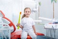 Child girl in white clothes at reception at a pediatric dentist smiles and laughs. little girl holds a big toothbrush in the