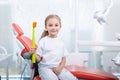 Child girl in white clothes at reception at a pediatric dentist smiles and laughs. little girl holds a big toothbrush in the Royalty Free Stock Photo