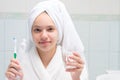 Child girl, in a white robe and towel on her head, in the bathroom, holding toothpaste, brush and a glass of water, close-up