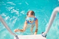 A child in goggles on the steps climbing out of the pool