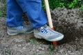 Child in gray shoes digging a hole with orange toy spade Royalty Free Stock Photo