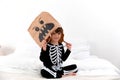 a child in a halloween costume sits with face mask on bed with white bedclothing