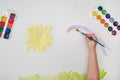 Child hand with brush drawing yellow sun on white paper Royalty Free Stock Photo