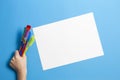 Child hand with colorful paintbrushes and blank white paper sheet on blue background