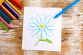 Child hand drawing Daisy Flower with wax crayons. Wood background