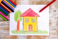 Child hand drawing House with wax crayons. Wood background