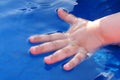 Child hand half dipped in water of blue plastic swimming pool Royalty Free Stock Photo