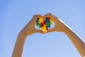 Child hand holding colorful heart on blue sky background. World autism awareness day concept