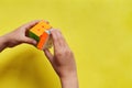 Child hand holding colorful Rubik`s cube on yellow background. Concept of play game and puzzle construction. Closeup, top view Royalty Free Stock Photo