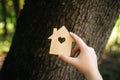 Flat wooden house shape in child hands against a forest background.