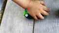 The child hand plays a green toy car on a gray wooden background Royalty Free Stock Photo