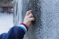 A child hand touching a mosaic of white black and grey tesserae in a street.