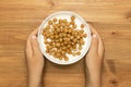 Child hands holding full bowl of yogurt with cereal breakfast balls on wooden table, top view. Quick and healthy food