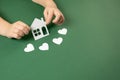 Child hands holding white paper house and heart on green background. Family home and real estate concept. Royalty Free Stock Photo