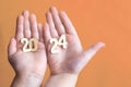 Child hands holding wooden number 2024 on palms on festive Peach Fuzz background with copy space