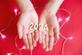 Child hands holding wooden number 2024 on palms on festive red background with copy space