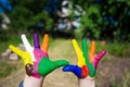 Child hands painted in bright colors isolated on summer nature background