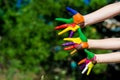 Child hands painted in bright colors on summer nature background