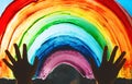 Child hands touch painting rainbow on window