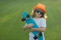 Child hold skateboard on a sunny day in the park. Outdoor portrait of little skateboarder. Child riding skateboard in