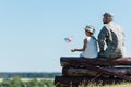 Child holding american flag near veteran father while sitting in fence