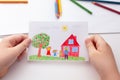 Child holding a drawing with a happy family and an apple tree and a house Royalty Free Stock Photo