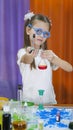 Child is holding flasks of colored liquid. Cute girl with blue round glasses on her face. Chemical experiments for