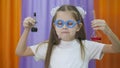 Child is holding flasks of colored liquid. Cute girl with blue round glasses on her face. Chemical experiments for