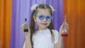 Child is holding flasks of colored liquid. Cute girl with blue round glasses on her face. Chemical experiments for