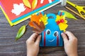 Child is holding Greeting card paper backpack on a wooden table. Handmade. Project of children`s creativity, handicrafts, crafts Royalty Free Stock Photo