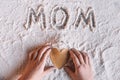 Child holding heart shaped cookie and word mom written in flour, Mothers day concept