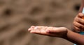 Child holding pebble in hand on sandy beach background Royalty Free Stock Photo