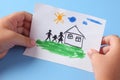 Child holds a drawn house with family