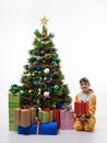 A child holds a gift while sitting by the Christmas tree