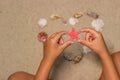 Child holds red starfish. Child hands with starfish. Sea shells on sandy beach. Summer background. Top view Royalty Free Stock Photo