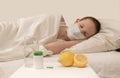 The child at home lies sick under a blanket with a temperature on his side close-up with lemon and medicine and a mask and virus