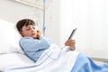 Child in hospital bed using smartphone surfs the internet wearing earphones