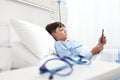 Child in hospital bed using smartphone surfs the internet wearing earphones Royalty Free Stock Photo