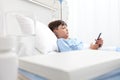 Child in hospital bed using smartphone surfs the internet wearing earphones Royalty Free Stock Photo